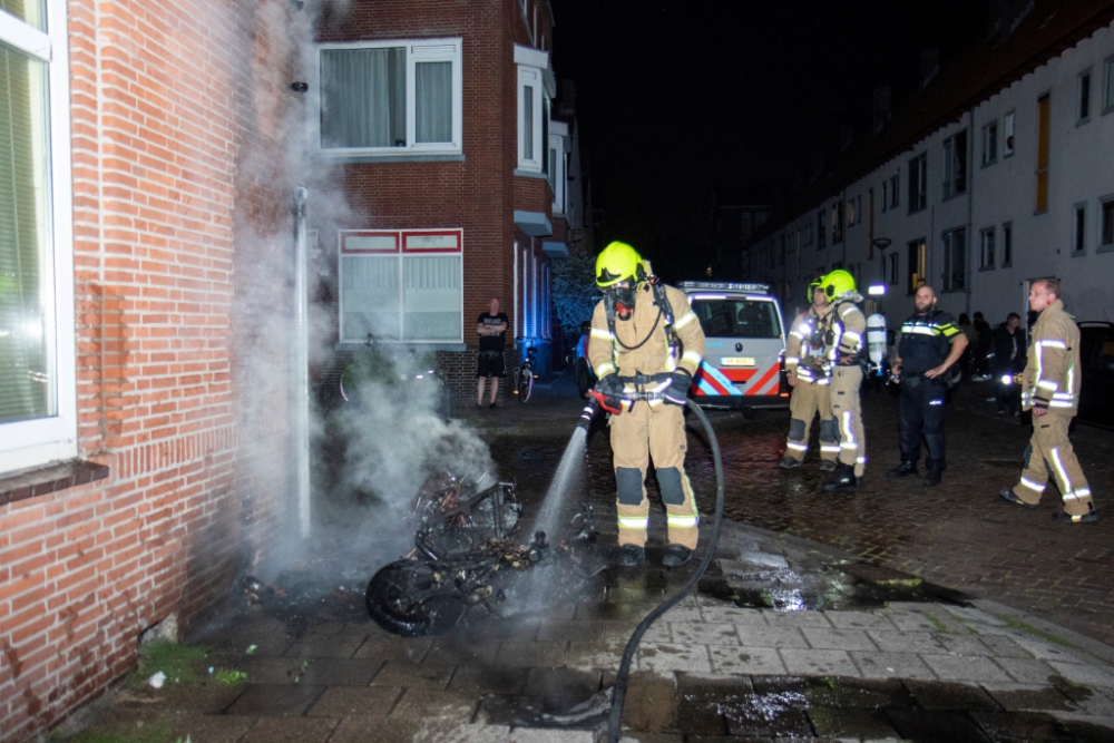 Scooter in brand tegen gevel van woning